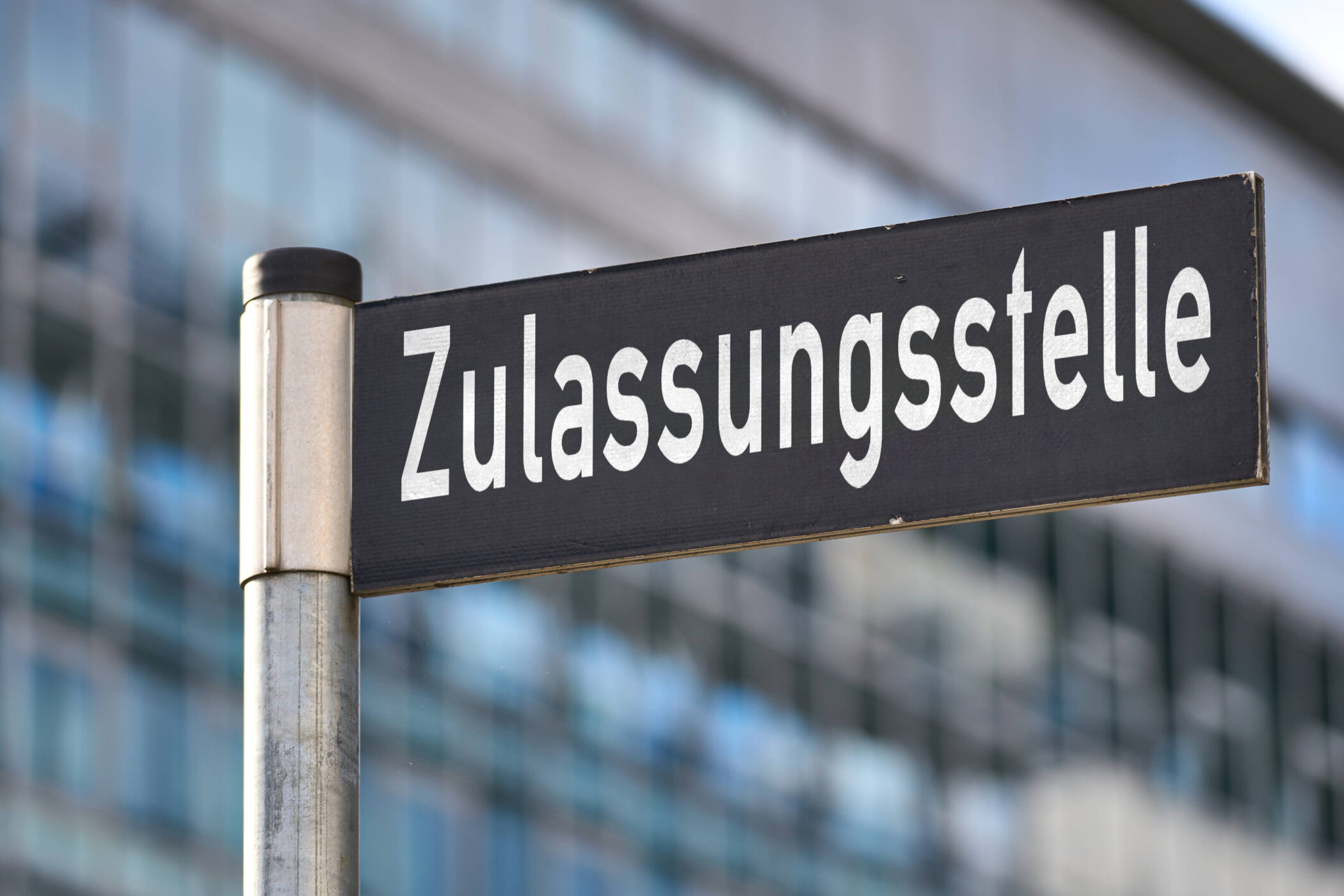 Schild mit der Aufschrift "Zulassungsstelle" vor unscharfem Hintergrund.