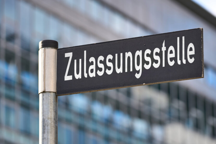 Schild mit der Aufschrift "Zulassungsstelle" vor unscharfem Hintergrund.