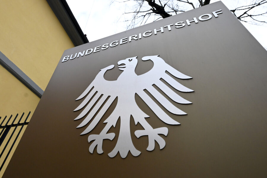 Schild mit Bundesadler und Text "BUNDESGERICHTSHOF", darunter ein Gebäude und Baum.