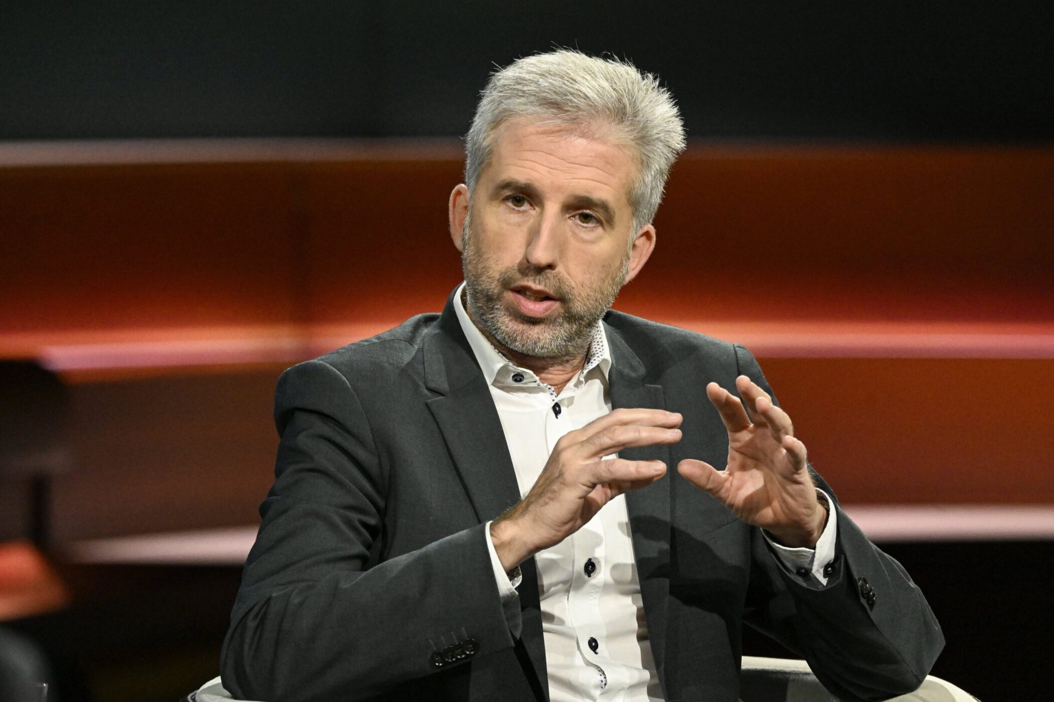 Ein Mann im Anzug spricht gestikulierend in einer Fernsehshow.