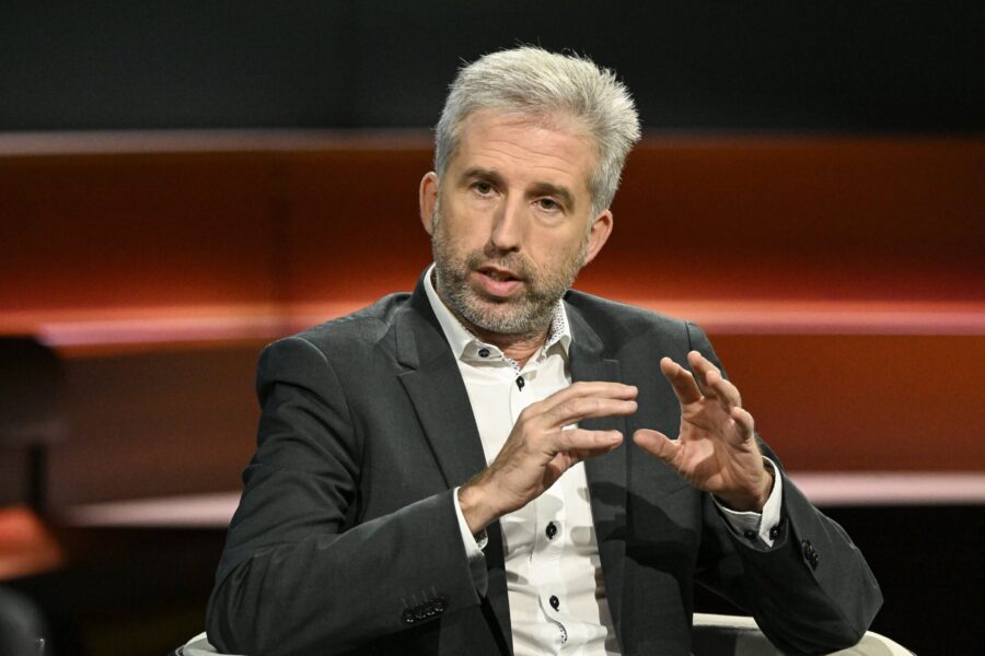 Ein Mann im Anzug spricht gestikulierend in einer Fernsehshow.