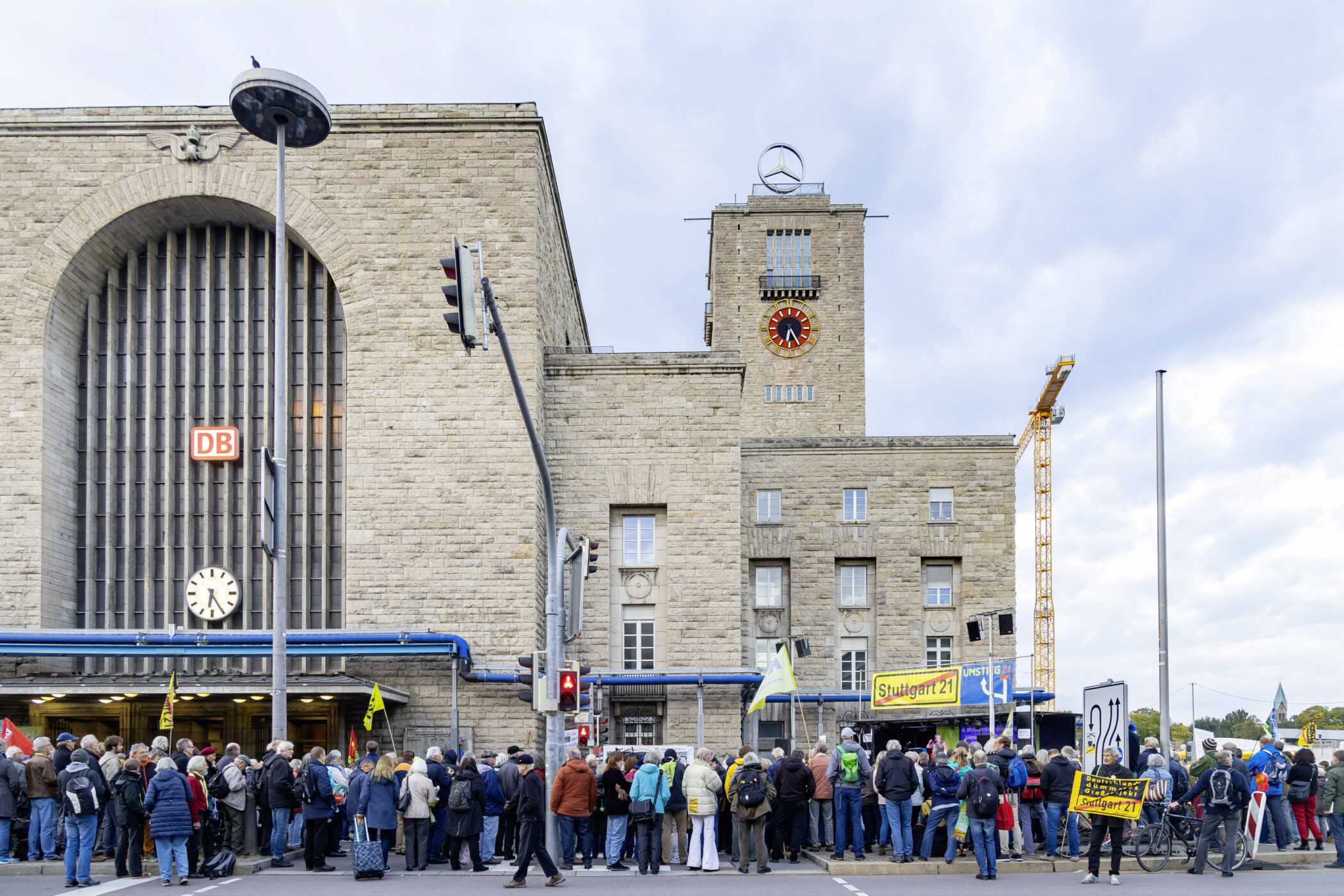 Menschenmenge vor einem Gebäude mit DB-Logo, einige halten Stuttgart 21-Schilder.