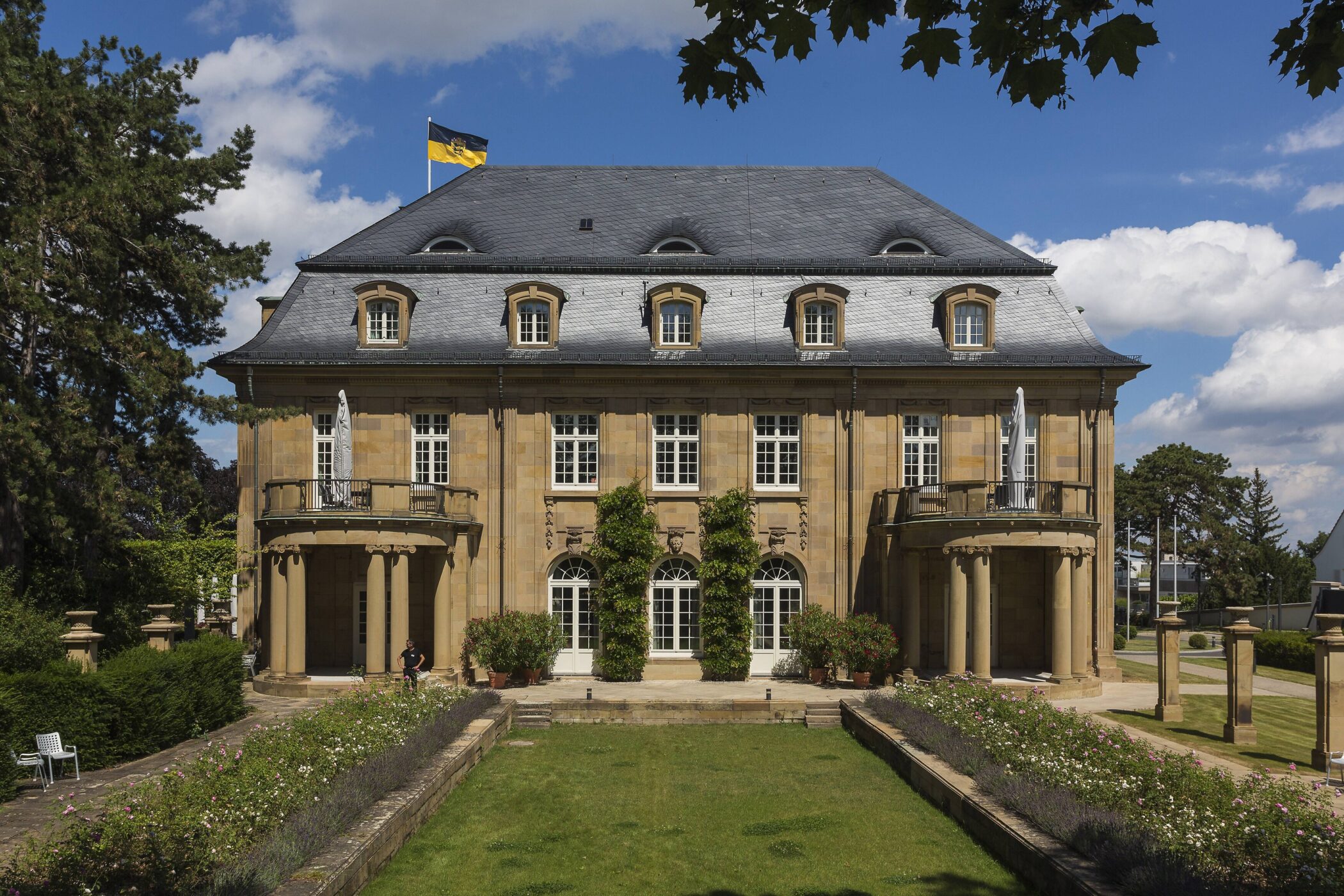 Großes Gebäude mit vielen Fenstern, zwei Terrassen und einem Garten im Vordergrund.