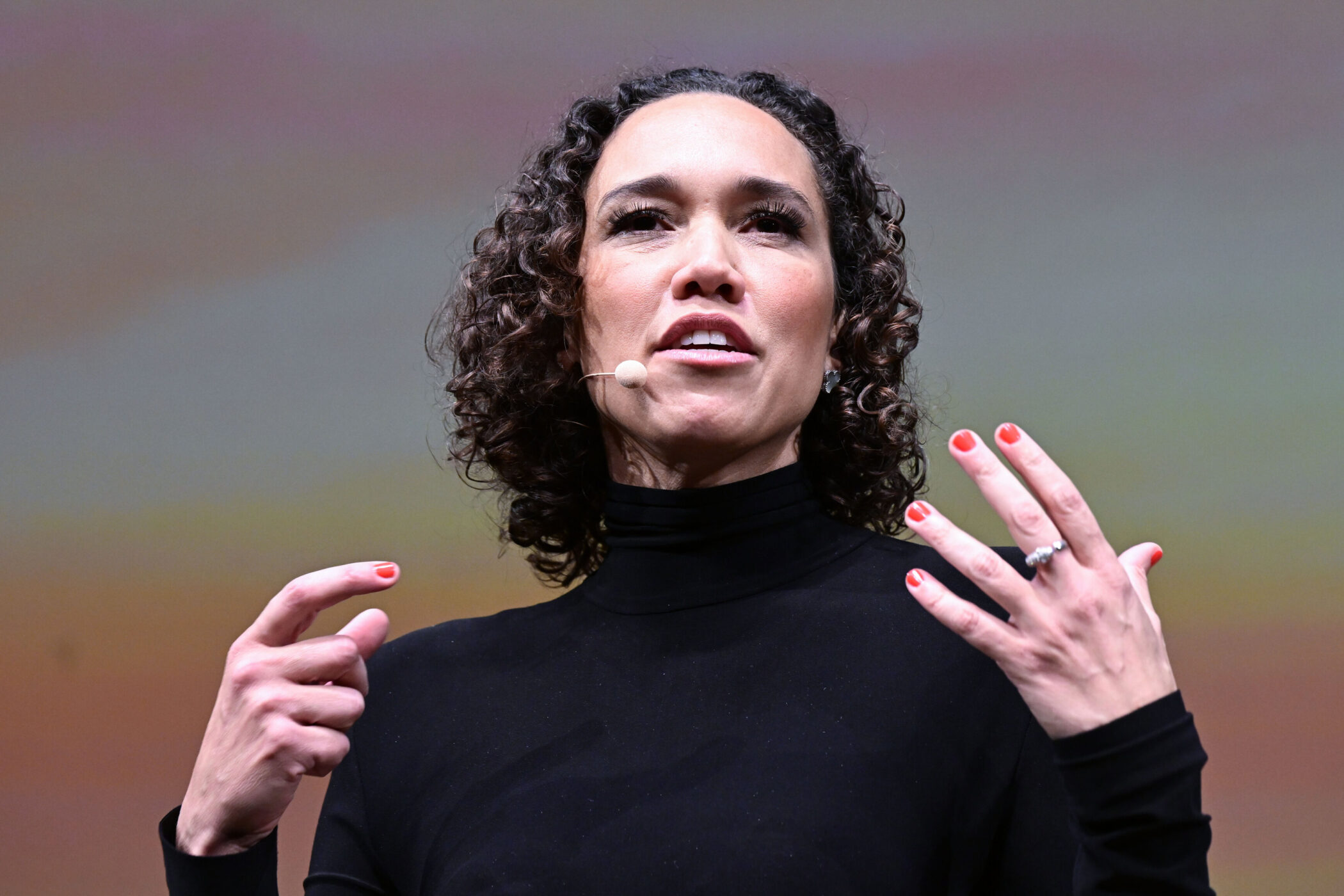 Person in schwarzem Oberteil mit Mikrofon, gestikuliert mit den Händen.