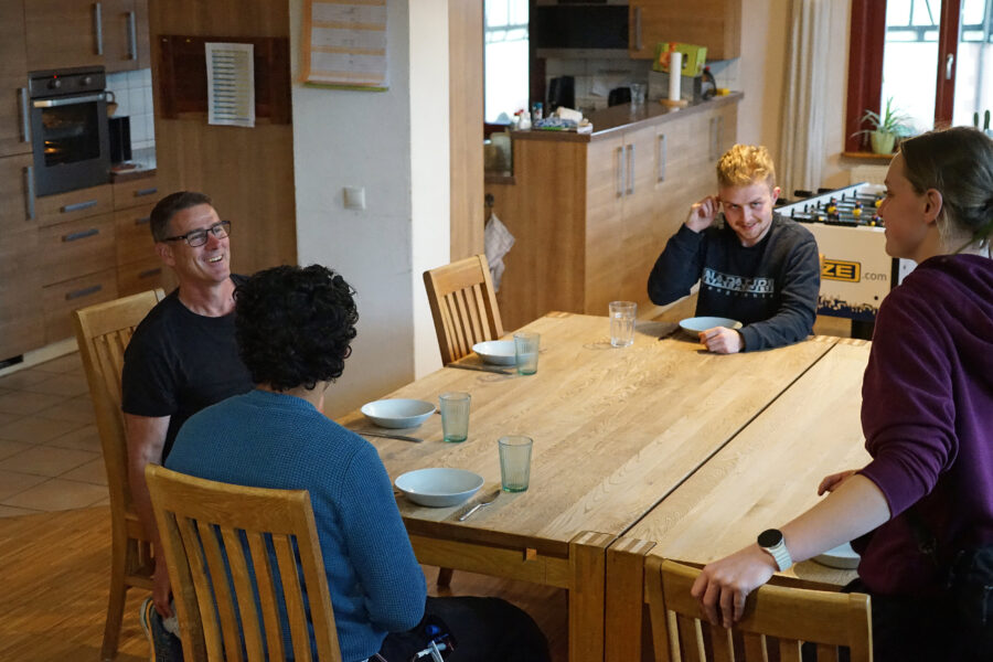 Vier Personen sitzen lachend an einem Tisch mit Gläsern und Schüsseln.