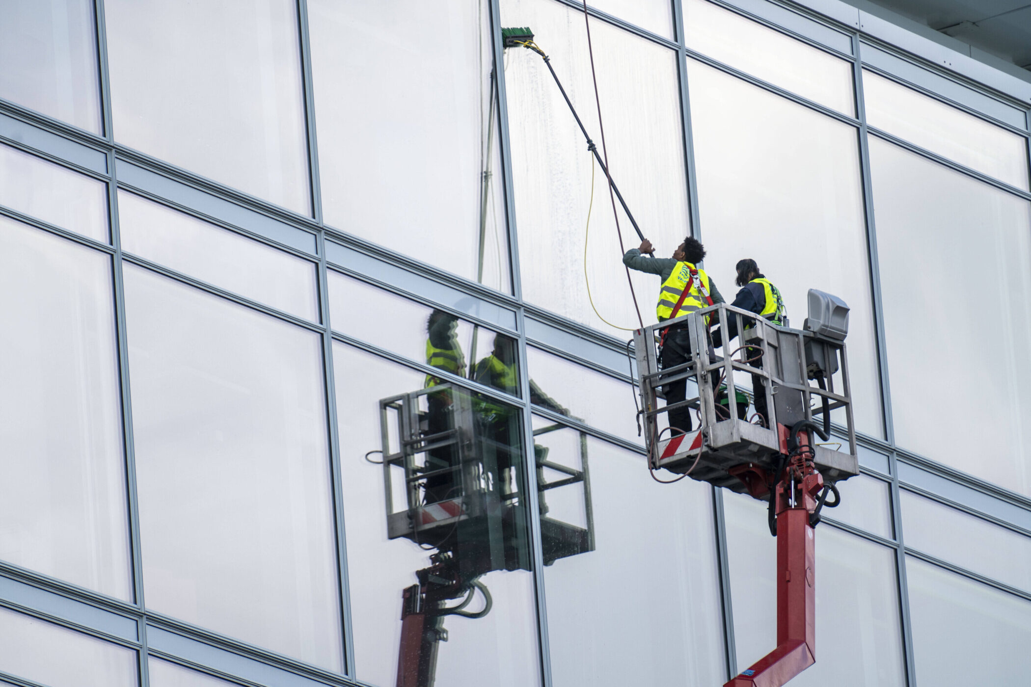 Zwei Personen reinigen Fenster eines Gebäudes von einer Hebebühne aus.