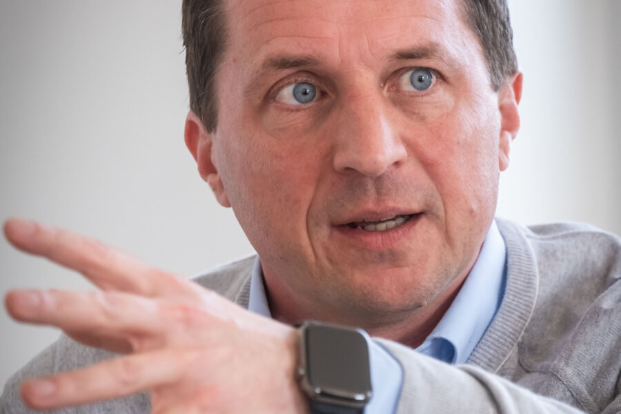 Ein Mann gestikuliert mit der Hand, trägt eine Uhr und ein helles Hemd.