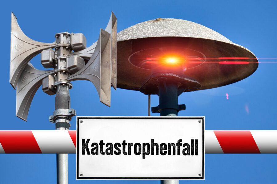 Zwei Sirenen und Schild mit "Katastrophenfall" vor blauem Himmel.