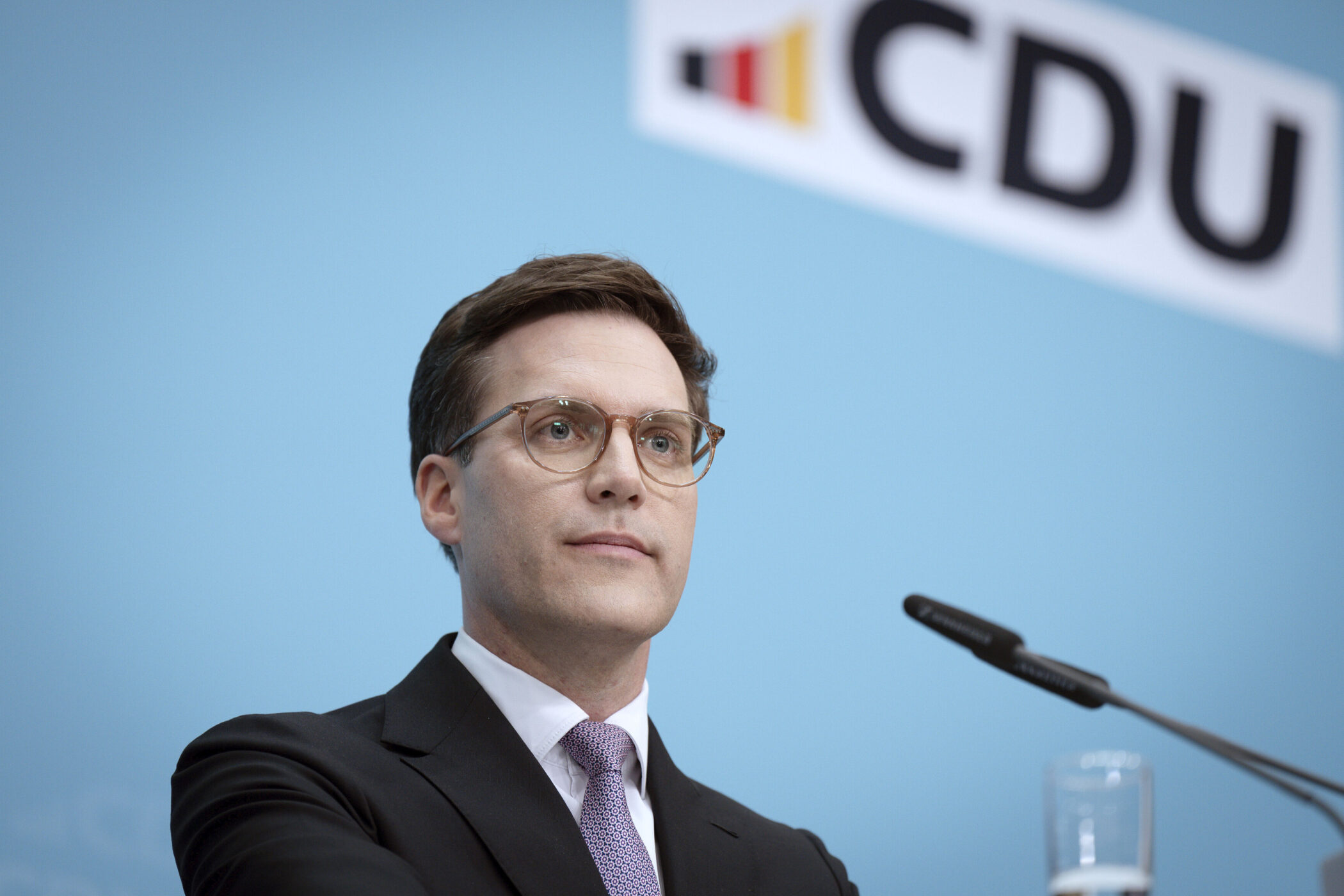 Ein Mann mit Brille spricht vor einem Mikrofon, CDU-Logo im Hintergrund.