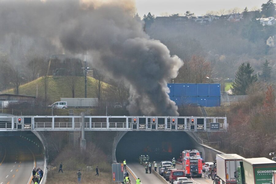 Dichter Rauch steigt aus einem Tunnel, Feuerwehrautos und Einsatzkräfte an der Zufahrt.