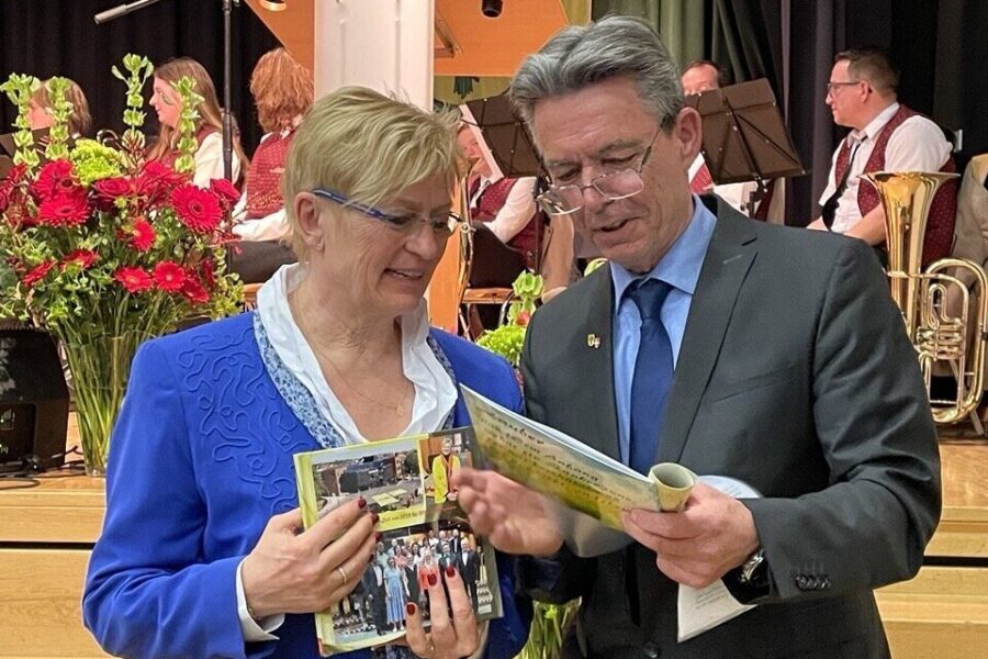 Zwei Personen betrachten Papiere, im Hintergrund sitzen Musiker.