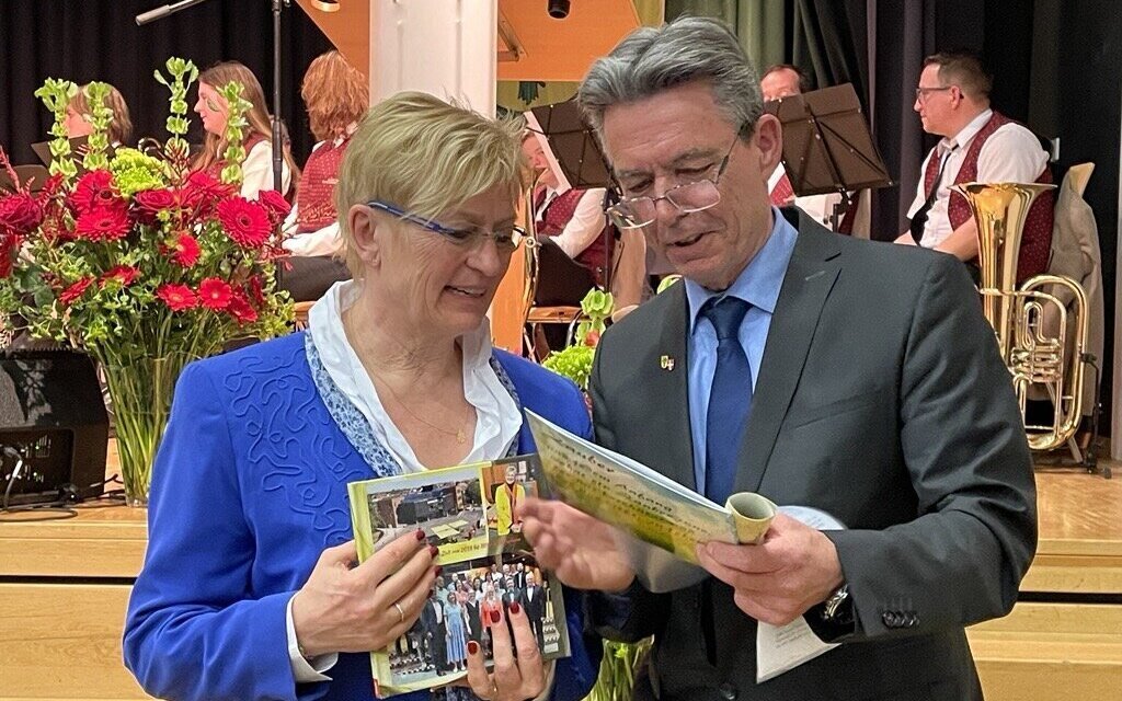 Zwei Personen betrachten Papiere, im Hintergrund sitzen Musiker.