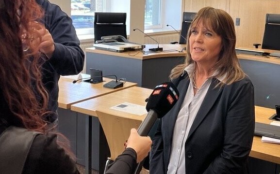 Zwei Personen, eine wird interviewt, Büroumgebung im Hintergrund.