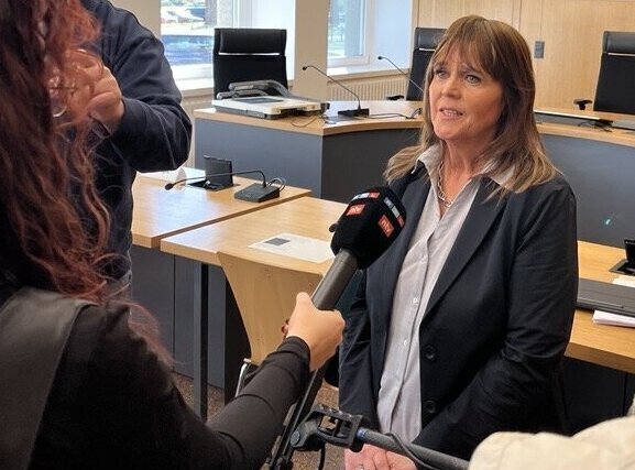 Frau in Anzug wird von Mikrofon vor Rednerpult interviewt.