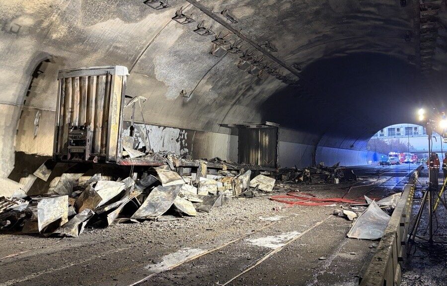 Verbrannter Lkw und Trümmer auf der Straße im Tunnel, Lichter im Hintergrund.