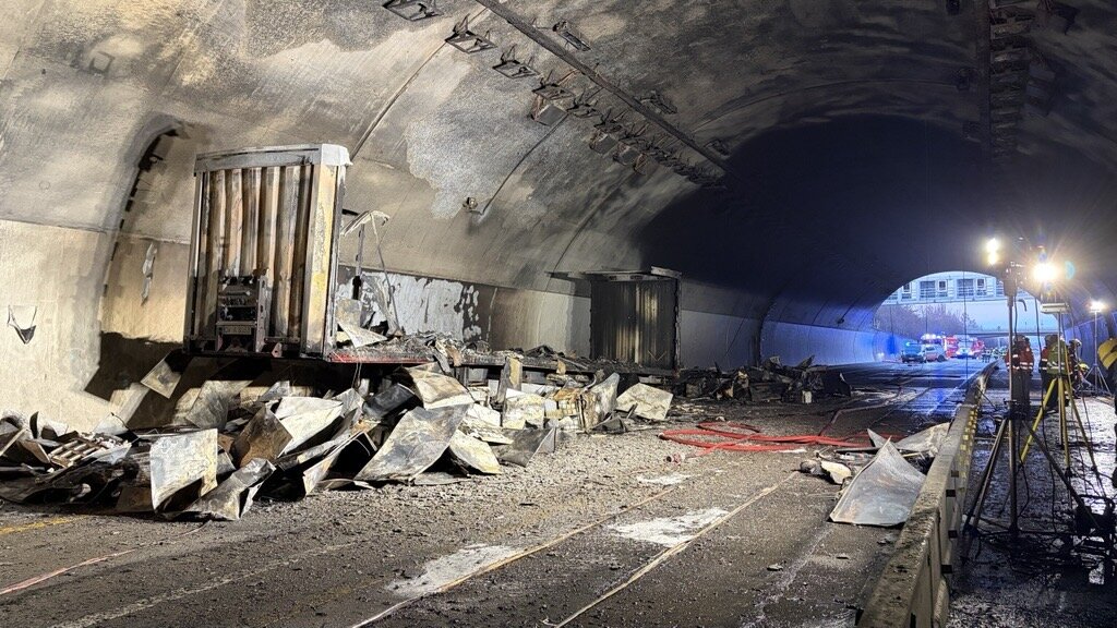 Verbrannter Lkw und Trümmer auf der Straße im Tunnel, Lichter im Hintergrund.
