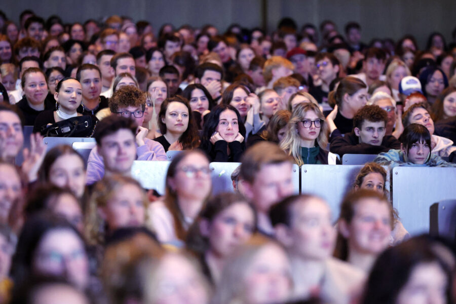 Zahlreiche Personen in einem Auditorium, nach vorne blickend.