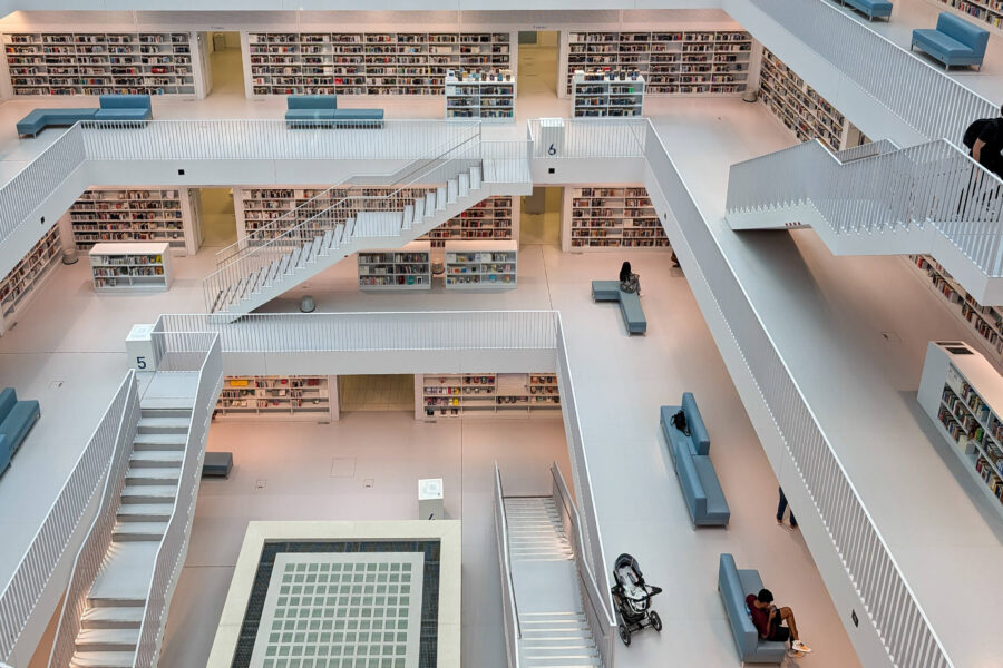 Große, moderne Bibliothek mit Regalen, Treppen und Sitzbereichen, Menschen verteilt.