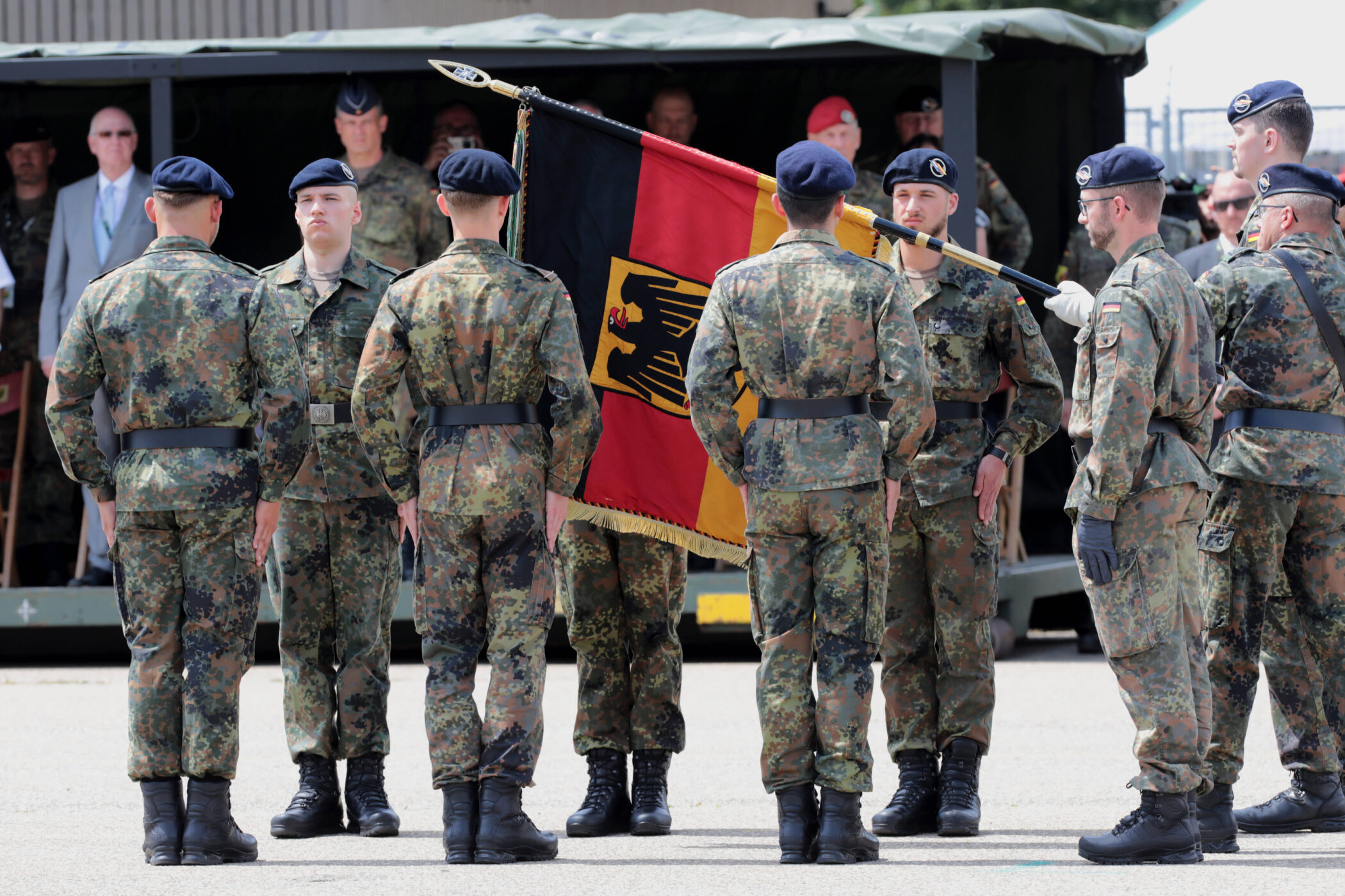 Soldaten in Tarnuniform mit deutscher Flagge, einige tragen Baskenmützen.