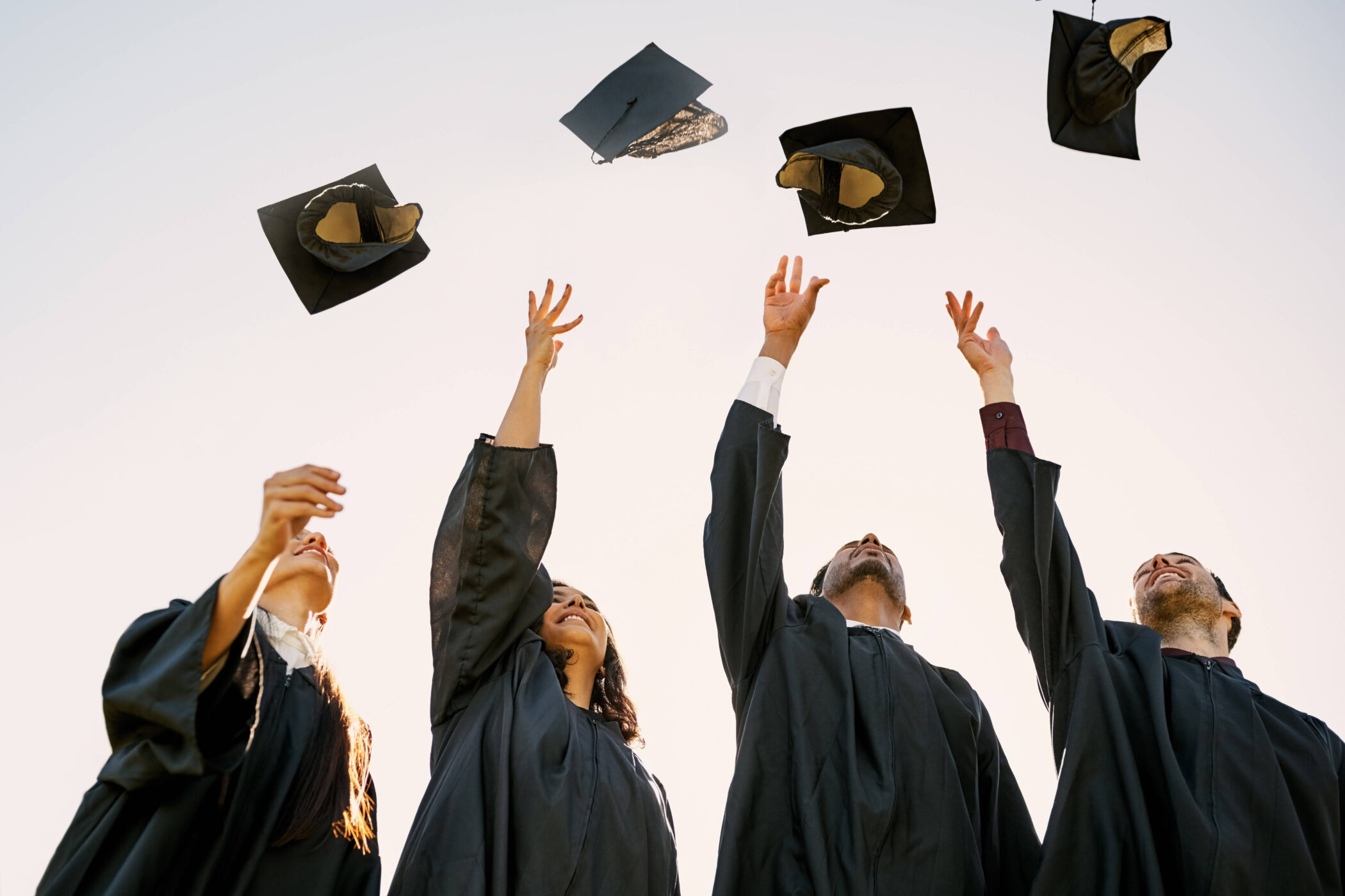 Vier Absolventen werfen Hüte in die Luft.