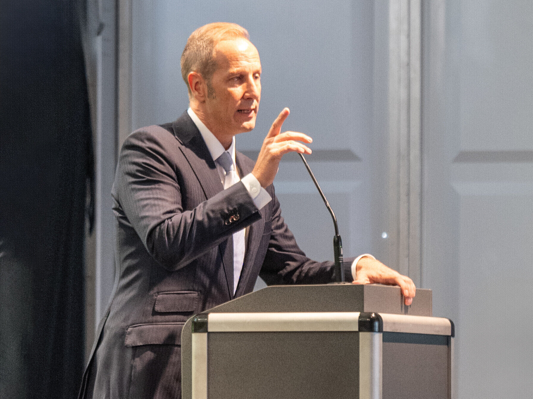 Mann im Anzug spricht an einem Rednerpult mit Mikrofon.
