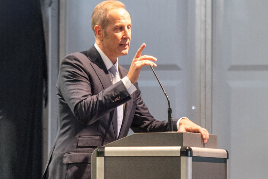 Mann im Anzug spricht an einem Pult mit Mikrofon.