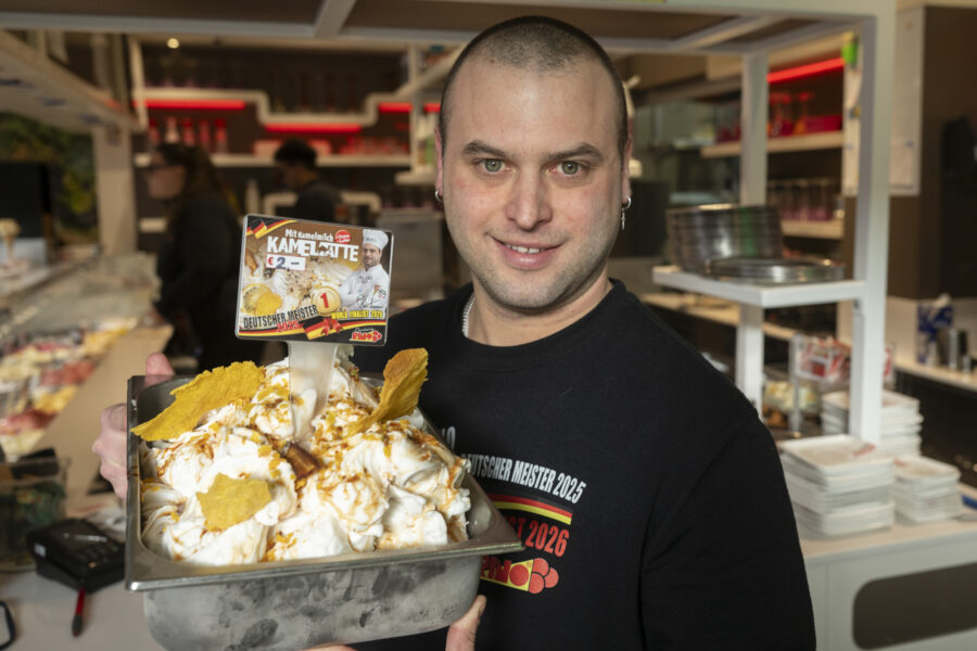 Mann hält Behälter mit Eis vor sich, im Hintergrund Eisdiele.