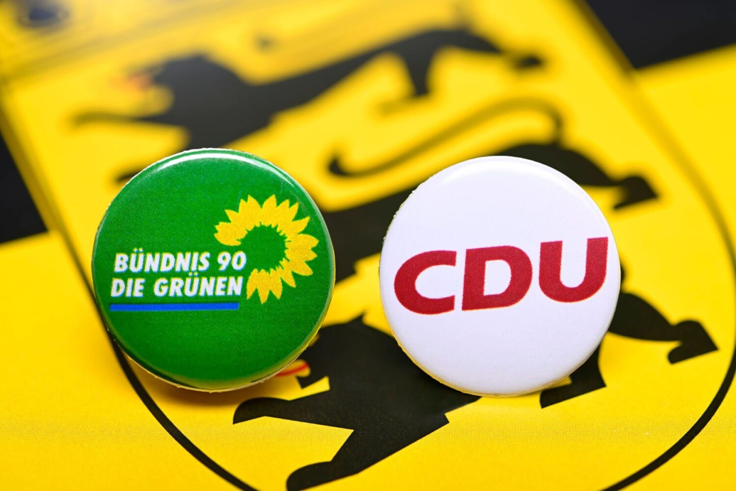 Zwei Buttons mit Logos von Bündnis 90/Die Grünen und CDU auf gelbem Hintergrund.