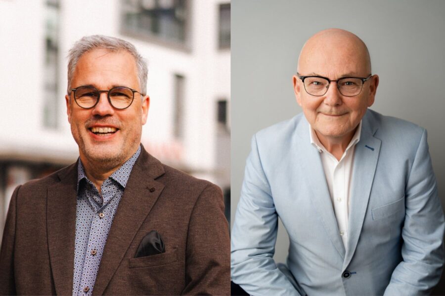 Zwei Männer mit Brillen in Anzügen, einer graumeliert und der andere glatzköpfig.