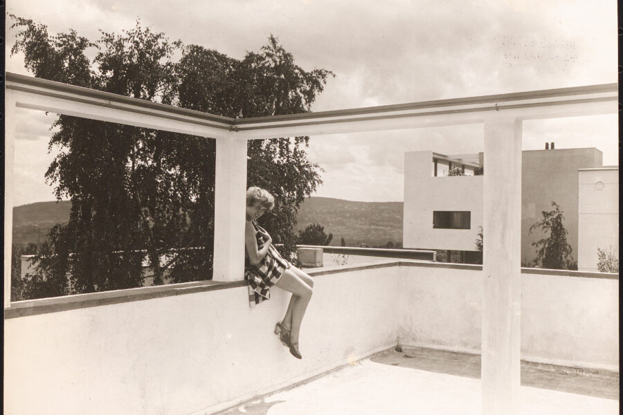 Person sitzt auf Brüstung in modernem Hof, im Hintergrund Bäume und Gebäude.
