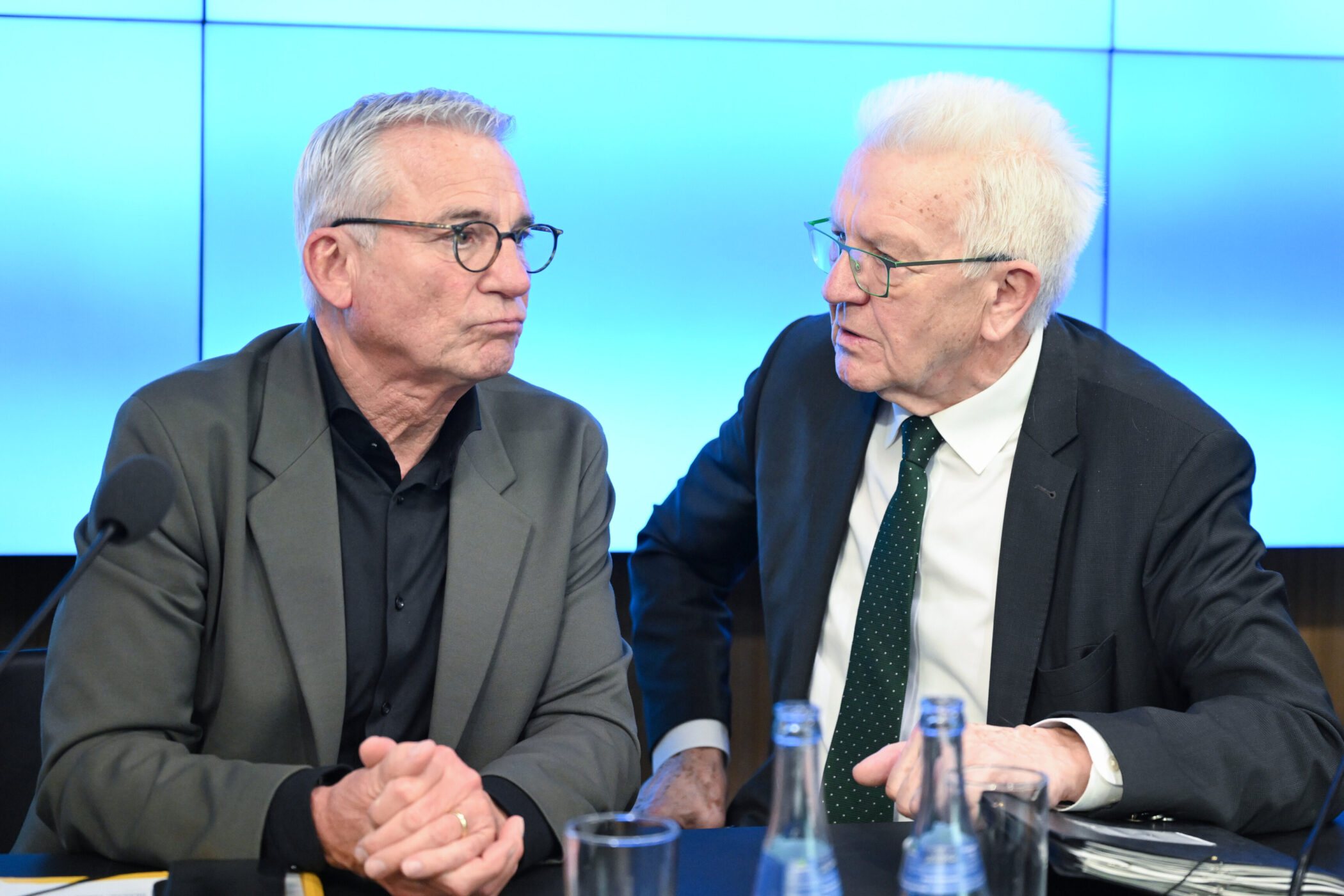 Zwei ältere Männer in Anzügen sitzen und unterhalten sich.