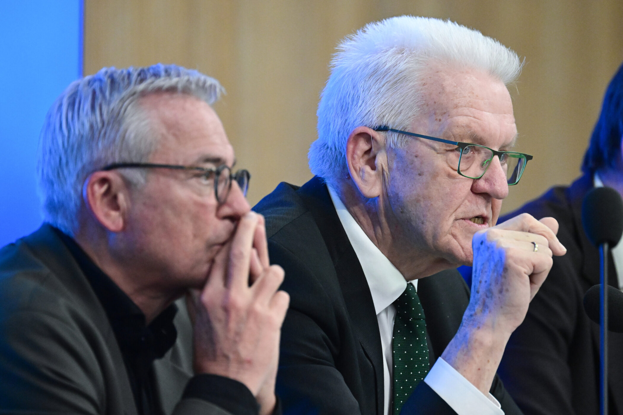 Zwei Männer mit Brillen sitzen nebeneinander vor Mikrofonen.