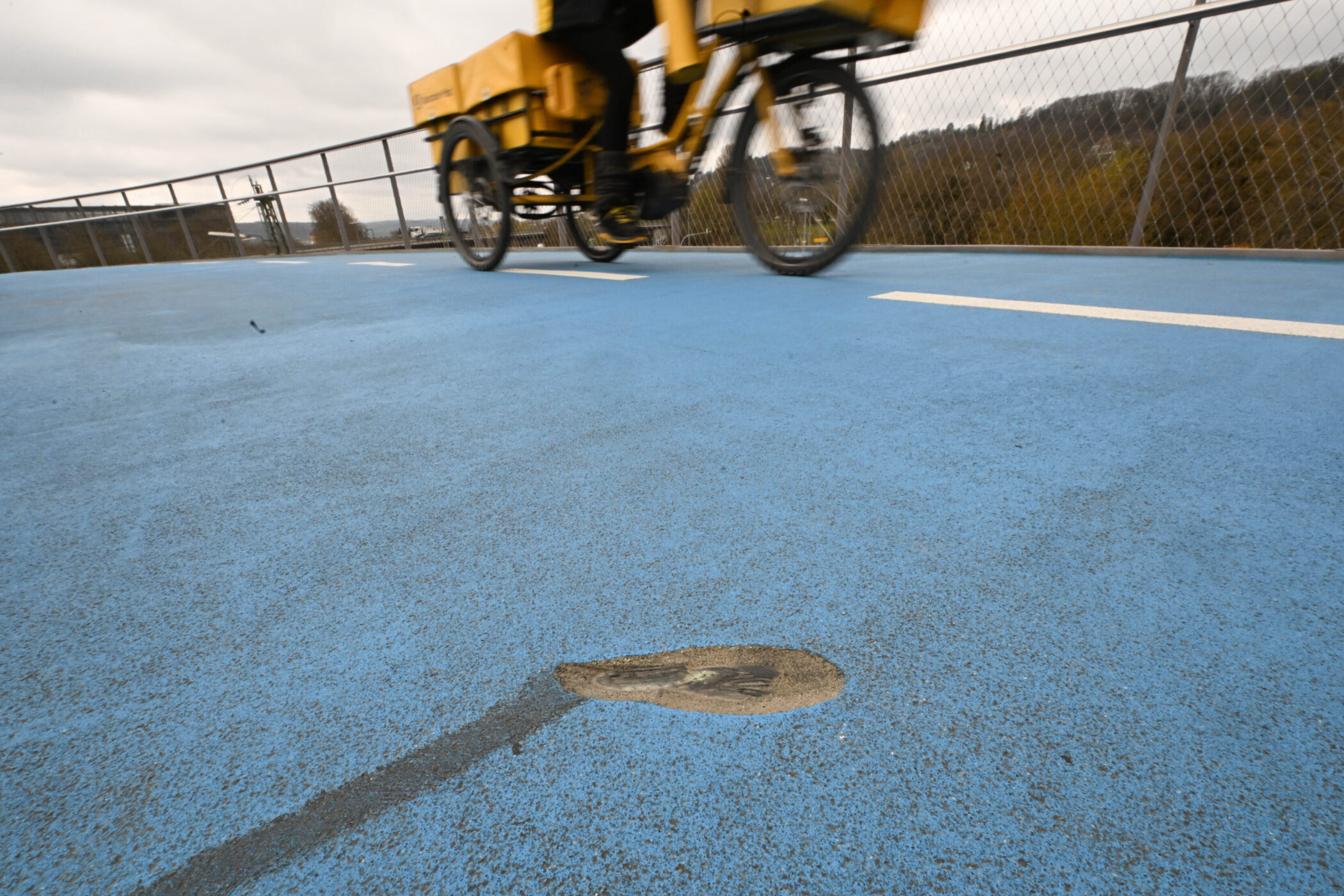 Gelbes Transportfahrrad auf blauem Weg mit weißer Linie und Schlagloch.