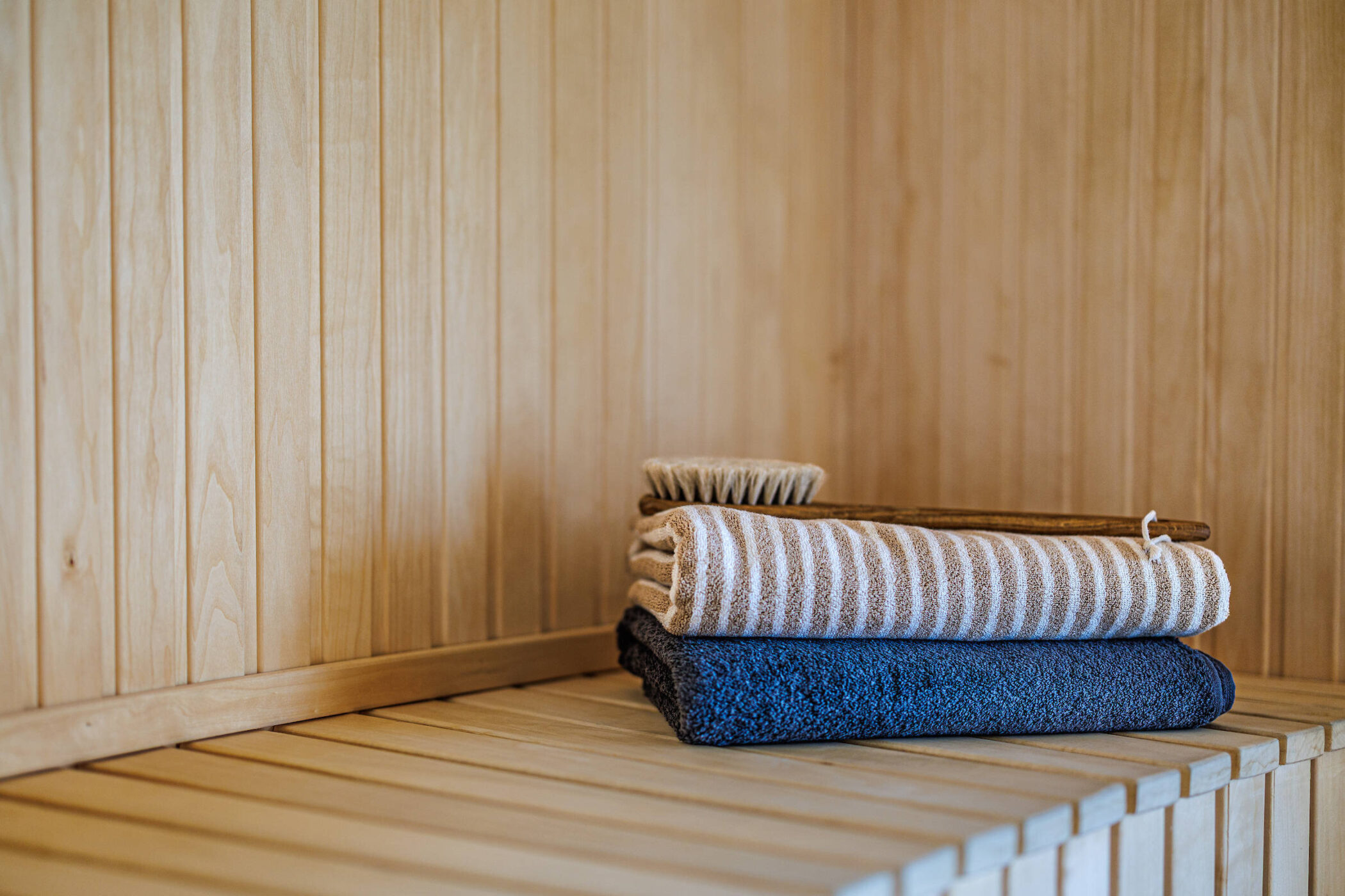 Gestreiftes Tuch, blaues Handtuch und Bürste auf Holzbank.