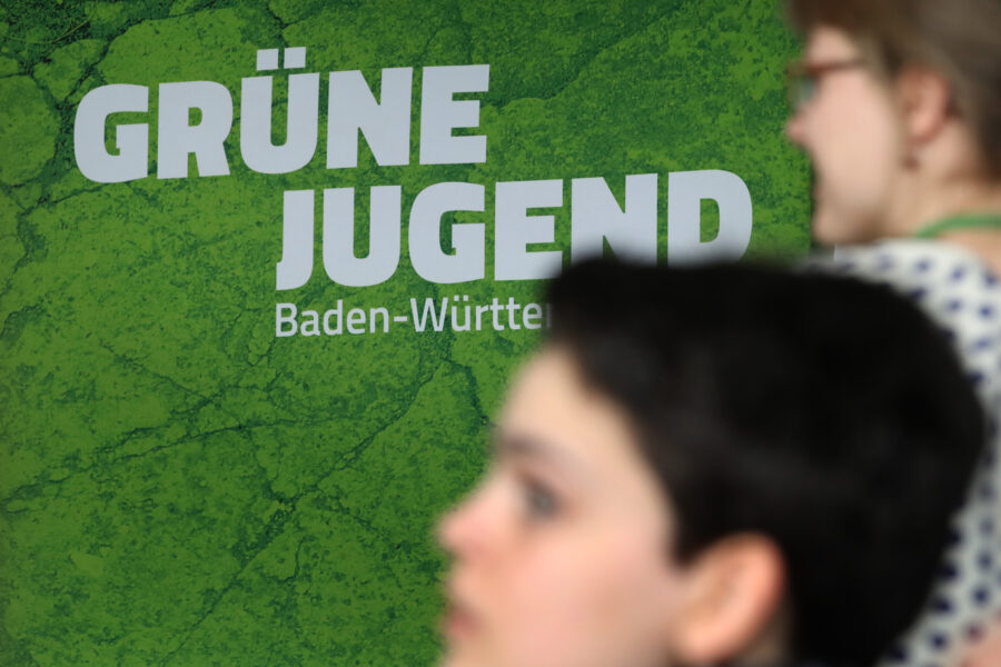Grüne Jugend Baden-Württemberg auf grünem Hintergrund, zwei Personen unscharf im Vordergrund.