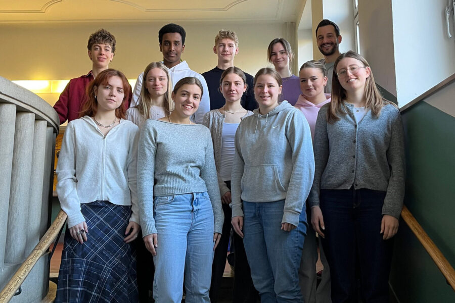 Zwölf Personen stehen auf einer Treppe und blicken in die Kamera.
