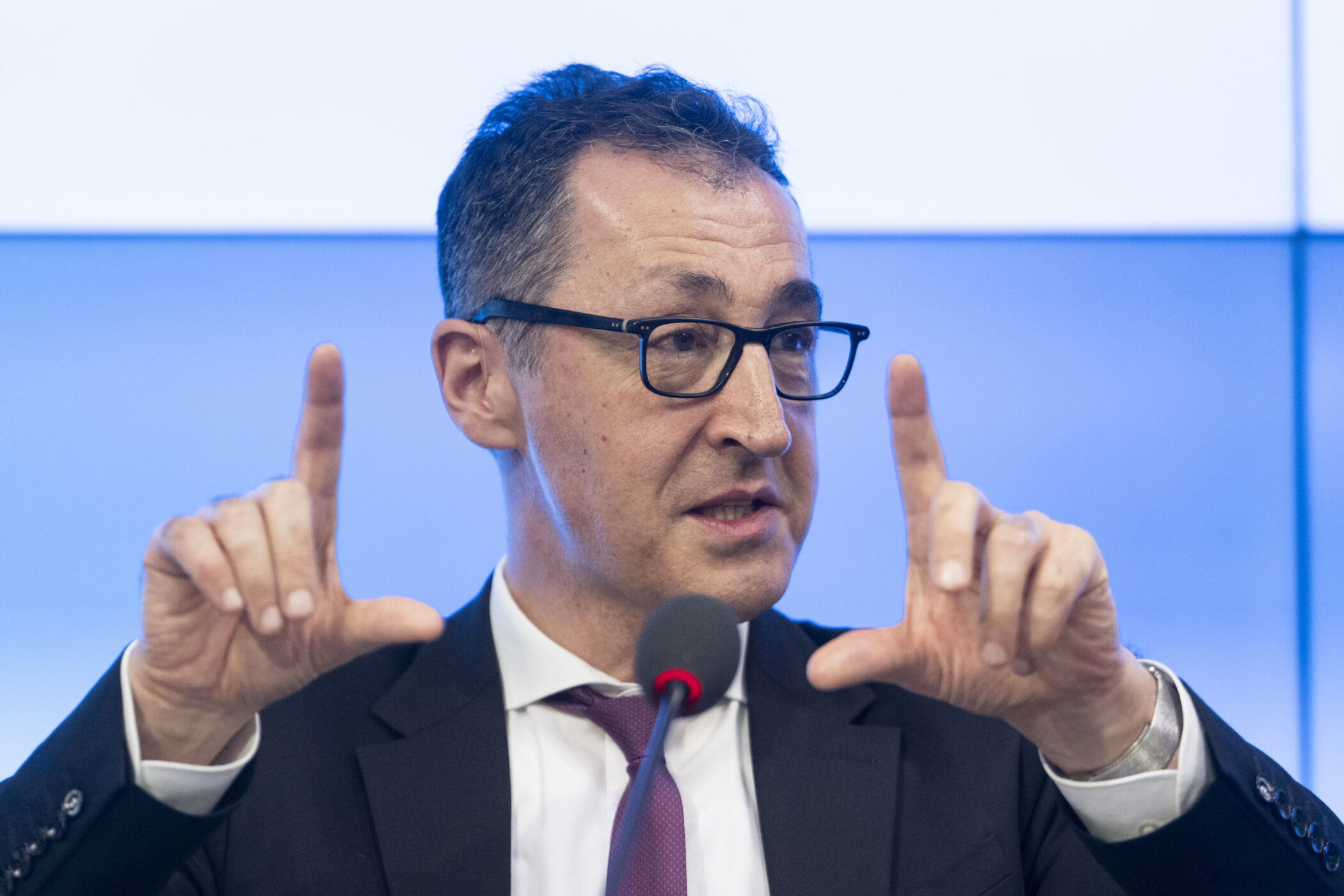 Mann mit Brille spricht, gestikuliert mit erhobenen Zeigefingern vor Mikrofon.