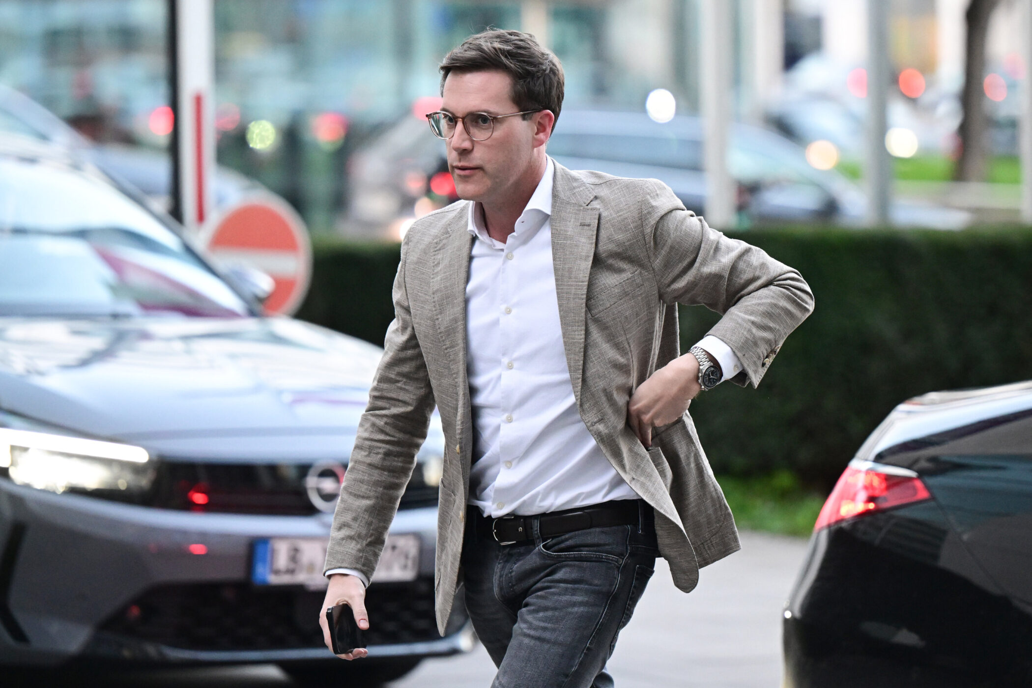 Ein Mann im Anzug geht über einen Parkplatz mit Autos im Hintergrund.