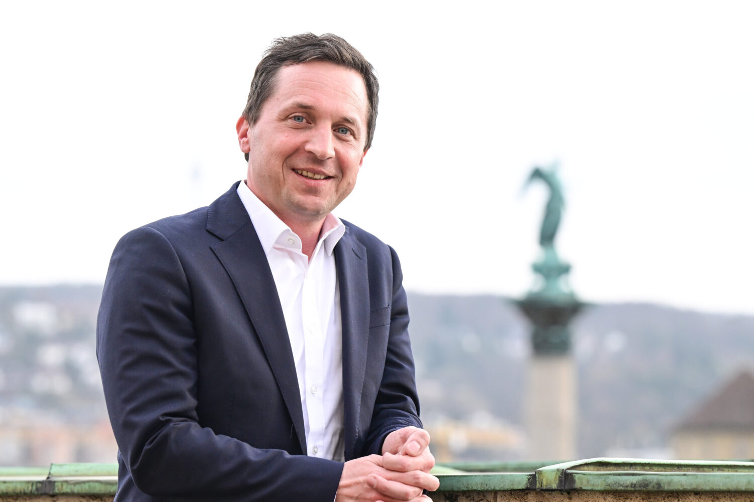 Mann in Anzug, lächelnd, vor unscharfem Hintergrund mit Statue.