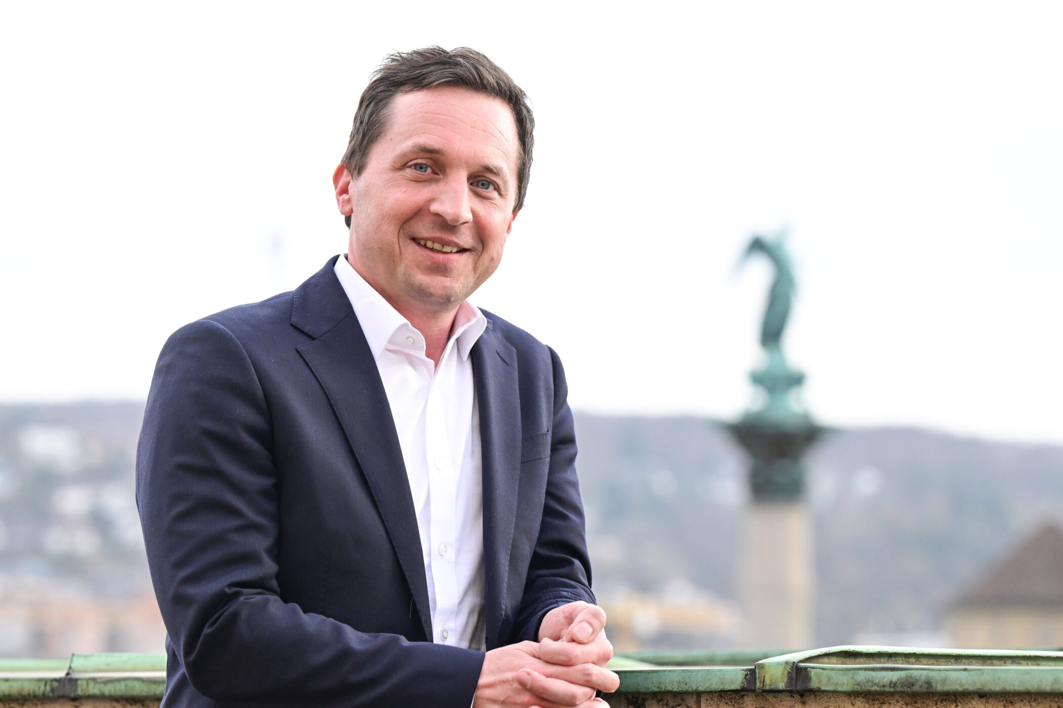 Mann in Anzug, lächelnd, vor unscharfem Hintergrund mit Statue.