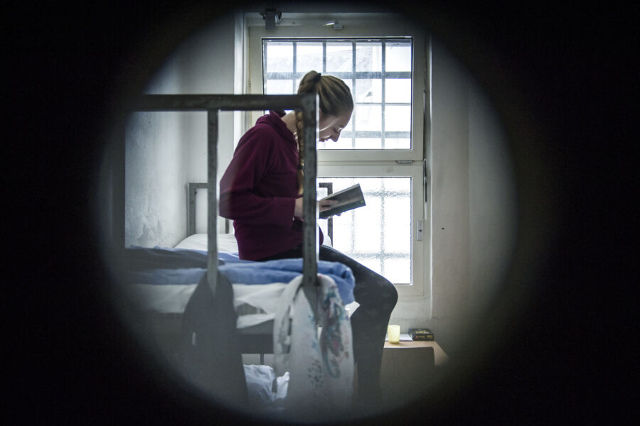 Person auf einem Bett in einem kleinen Raum liest ein Buch bei Tageslicht.