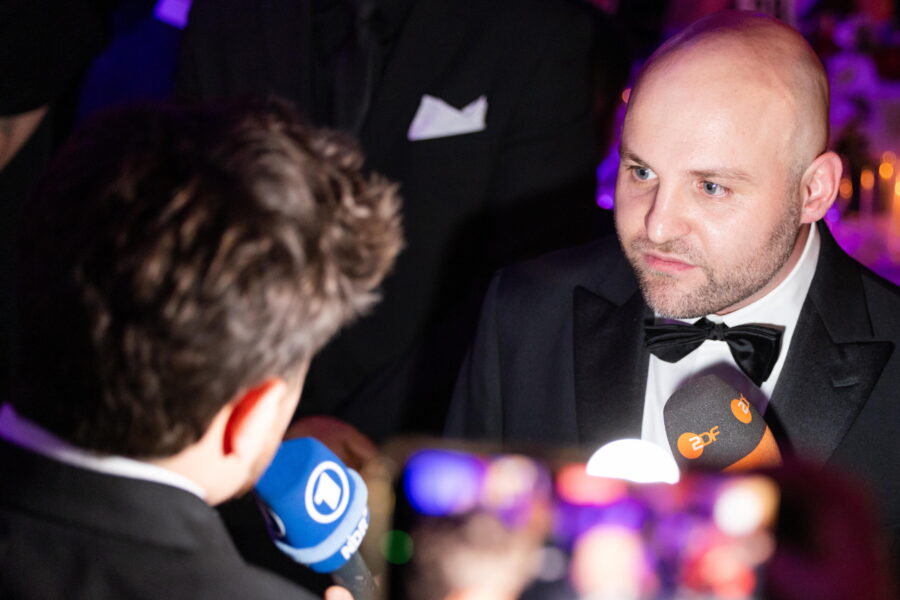 Zwei Männer in Anzügen, einer hält ein ARD-Mikrofon, der andere ein ZDF-Mikrofon.