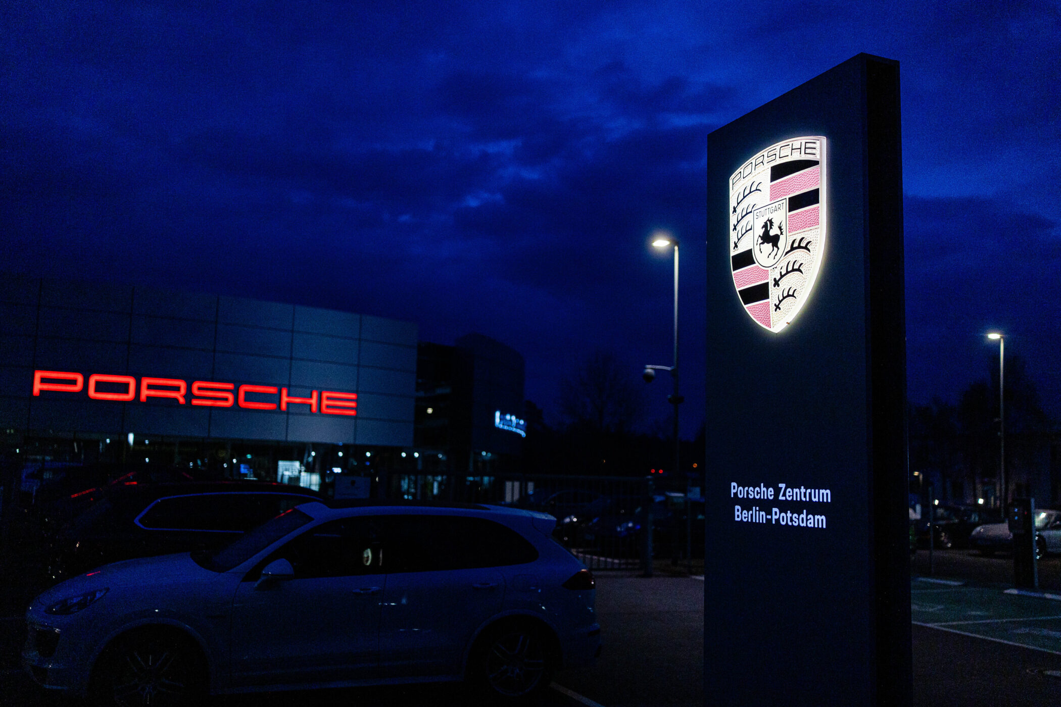 Leuchtendes Porsche-Logo, Schild mit "Porsche Zentrum Berlin-Potsdam", Auto im Vordergrund.