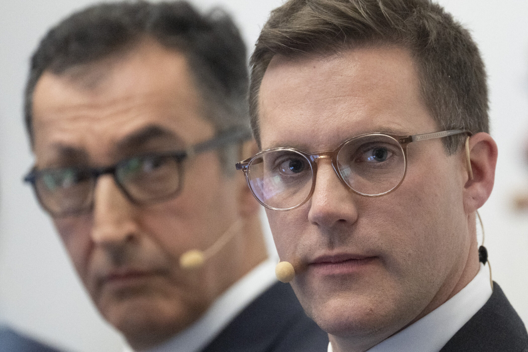 Zwei Männer mit Brillen und Headsets blicken ernst.