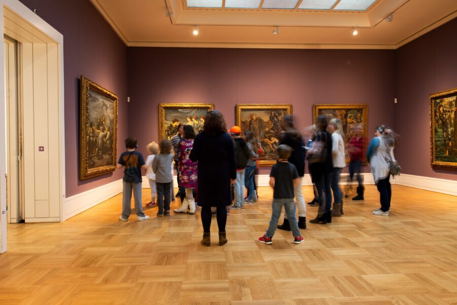 Gruppe Menschen betrachtet Gemälde in einem Museum. Holzboden, violette Wände.