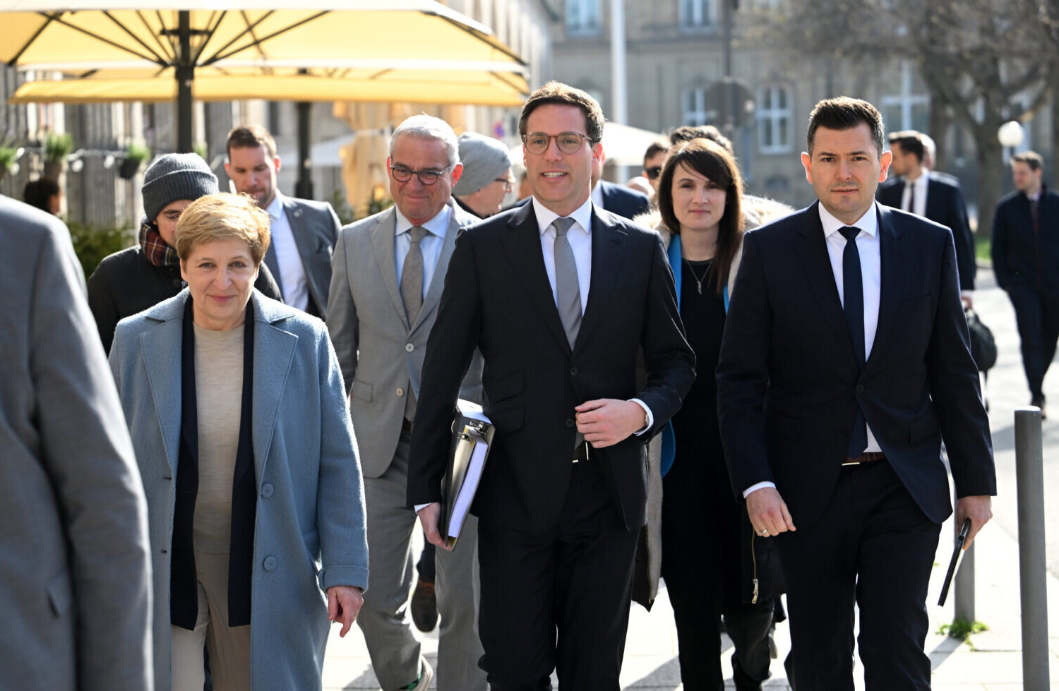 Mehrere Menschen in Anzügen und Mänteln gehen draußen.