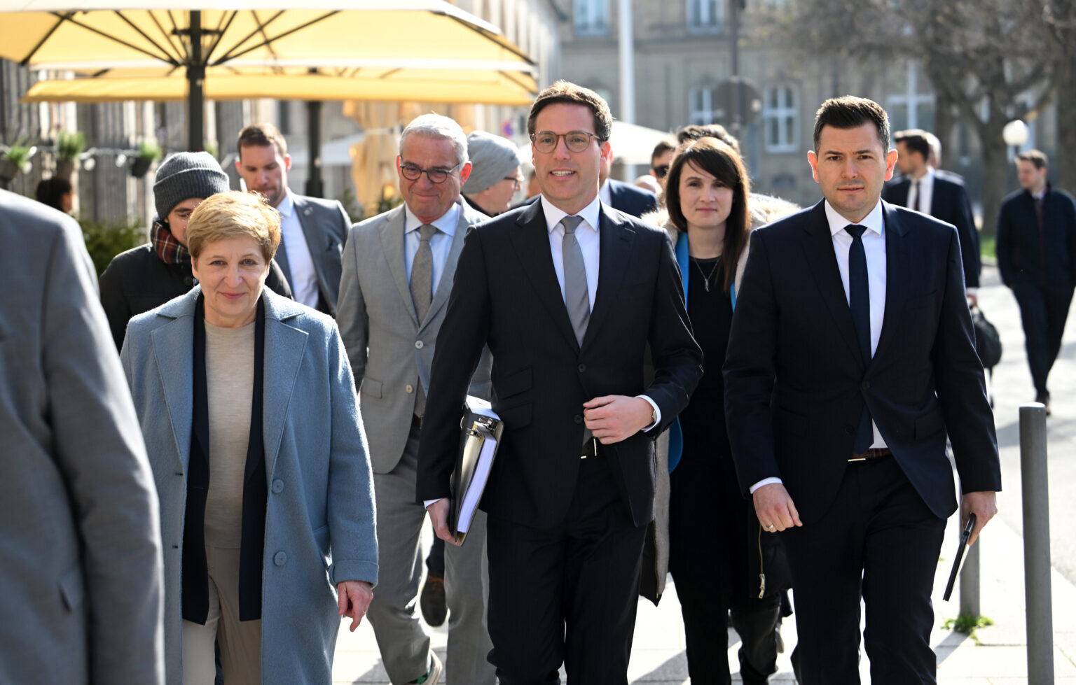 Mehrere Menschen in Anzügen und Mänteln gehen draußen.