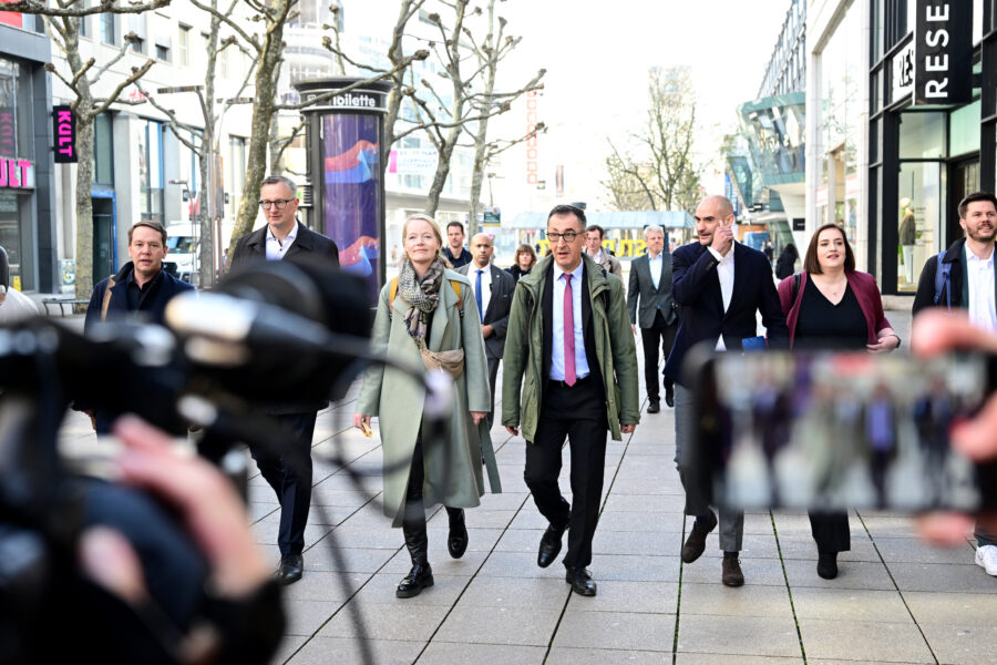 Gruppe von Menschen geht eine Einkaufsstraße entlang, Smartphone im Vordergrund.