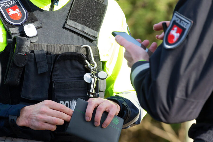 Zwei Polizisten in Uniform, einer hält ein Smartphone, der andere ein Dokument.