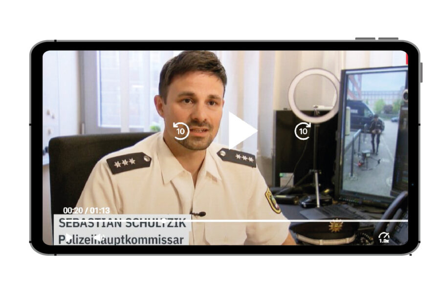 Mann in Polizeiuniform spricht in einem Büro, mit Monitoren im Hintergrund.